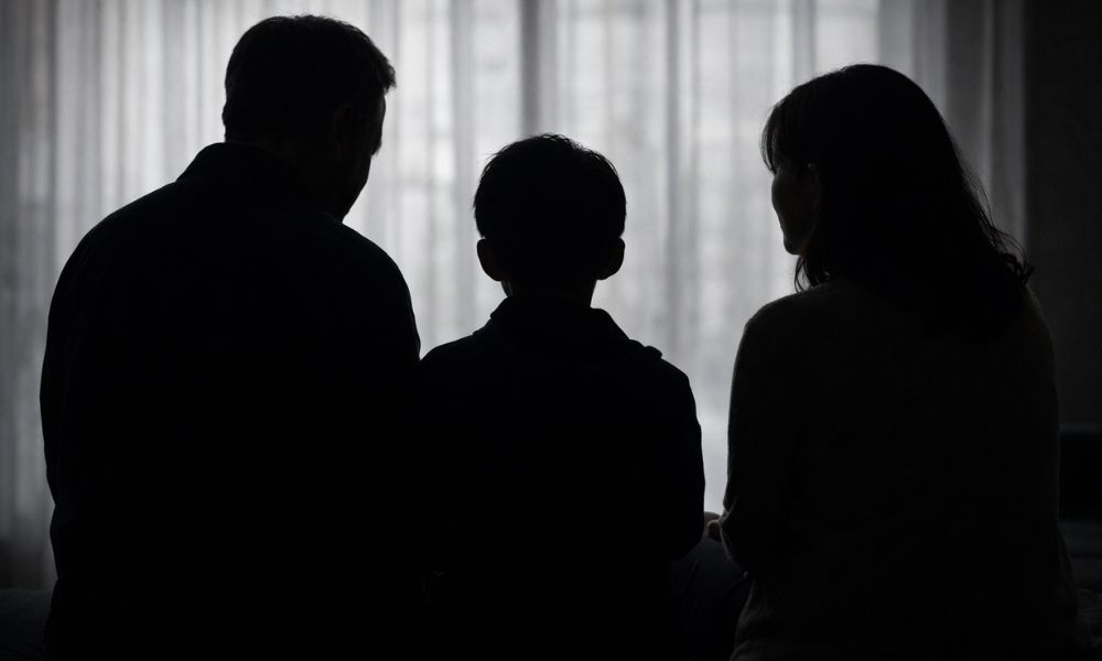 父親と母親に挟まれて座る小学生の男の子の後ろ姿をシルエットで表現した家族イメージ画像