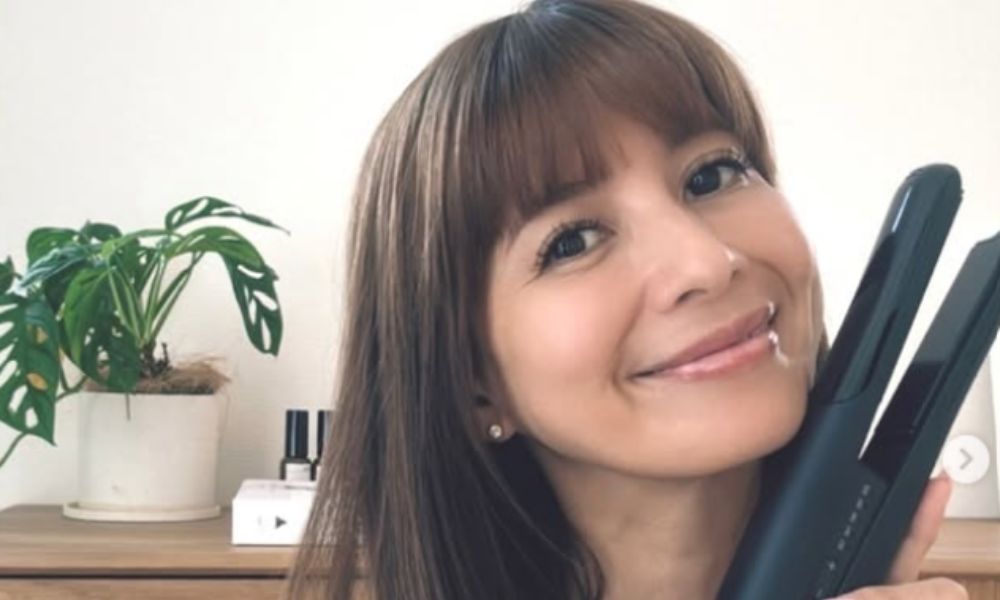 吉川ひなのが室内で微笑みながらヘアアイロンを手に持つナチュラルなポートレート。