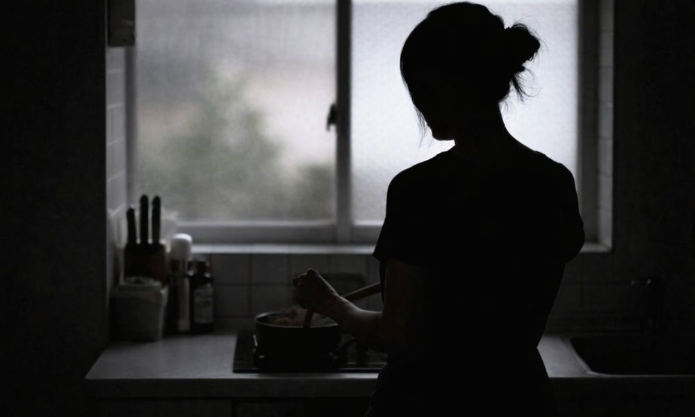 キッチンで料理をする女性の後ろ姿シルエット（窓の逆光で人物が黒く浮かび上がるイメージ）